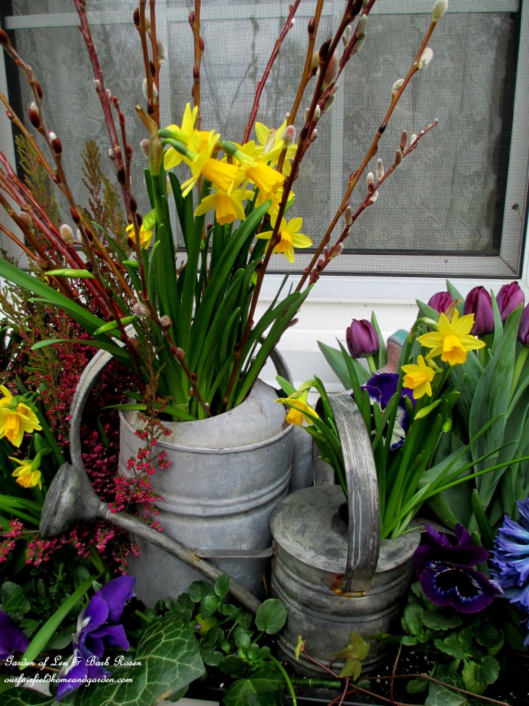 Close-up of the watering cans in the windowbox. https://ourfairfieldhomeandgarden.com/diy-project-welcome-spring-time-to-change-the-window-boxes/